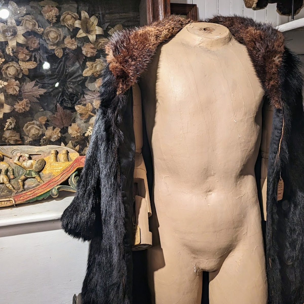 A male mannequin wearing a feathered, animal fur smoking jacket.