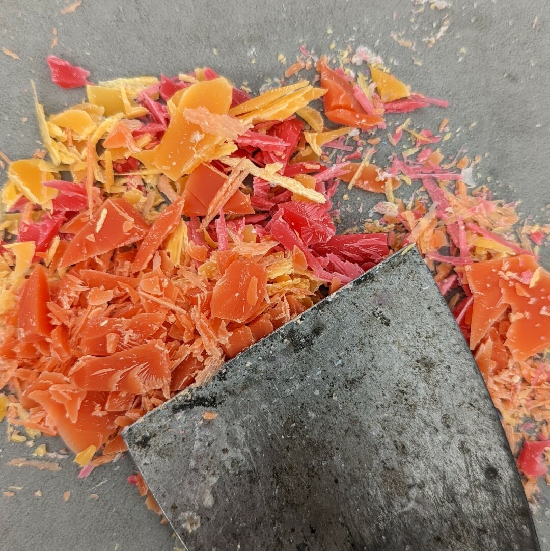 A metal putty knife and scraps of multi colored wax chips