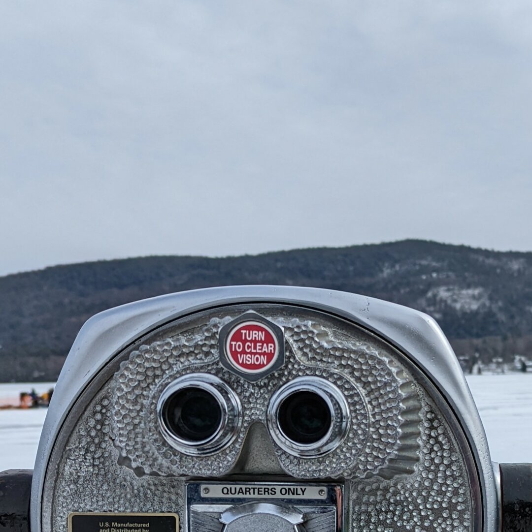 looking out over top of one of those paid tourist binoculars with a snow covered, iced over lake with a mountain in the background.