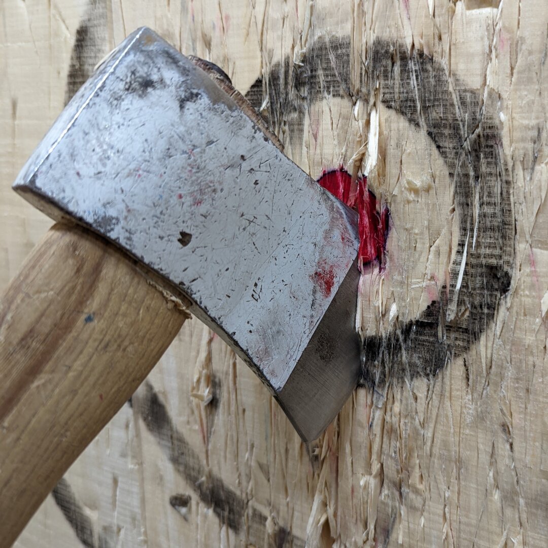 An axe stuck in the middle of the red bullseye on a plywood target