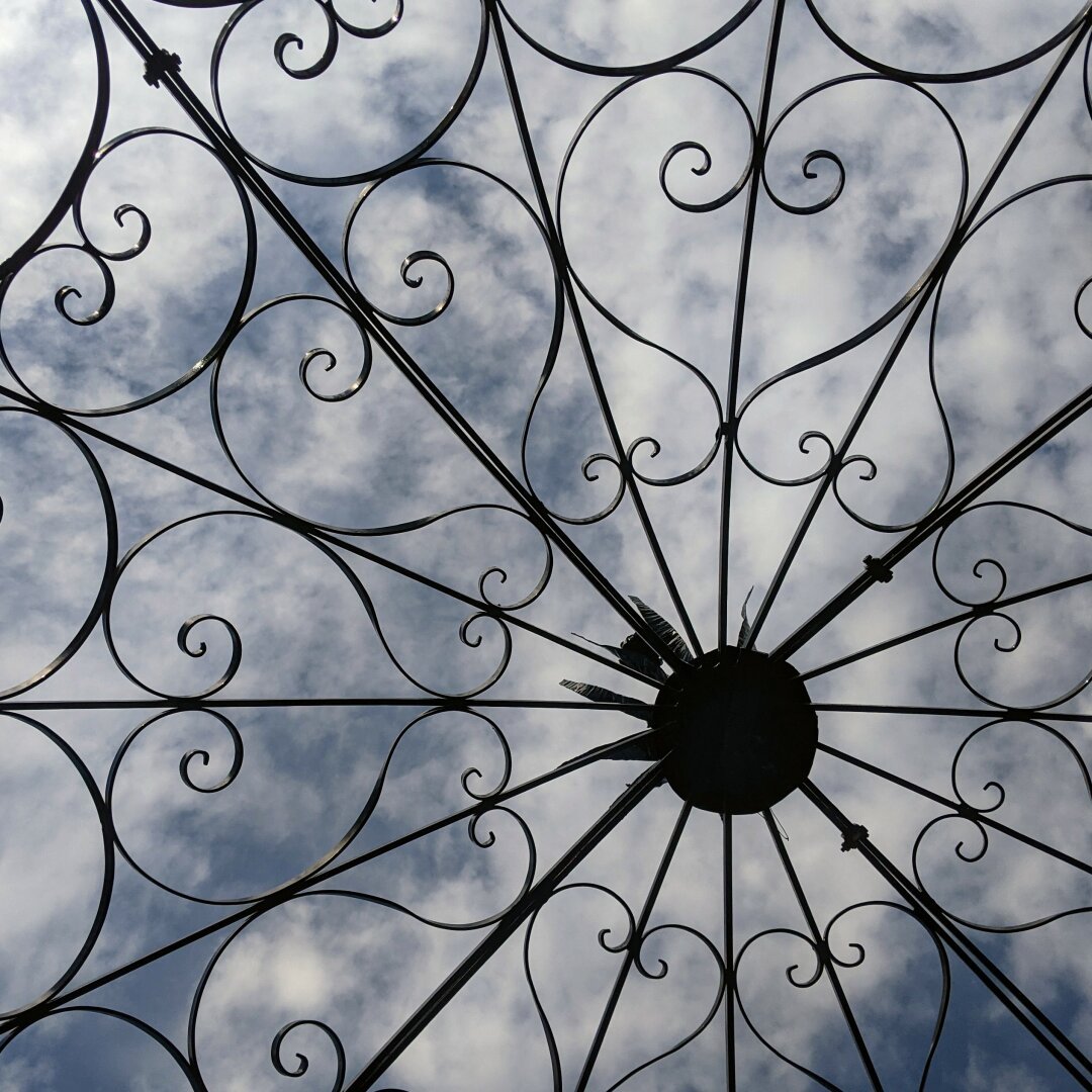 A metal wire canopy with clouds in the background