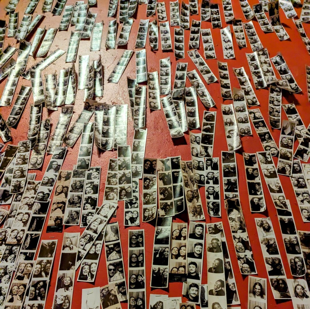 Hundreds of photobooth strips taped to a bright orange wall