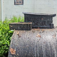 a gray cylindrical tank with grease dripping down the sides, fallen leaves stuck to it.