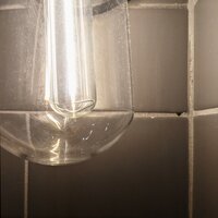 Close up of an old lightbulb filament with gray bathroom tiles in the background