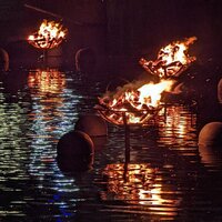 Elevated firepits above the river water in flames casting shadows on the ripples in the water