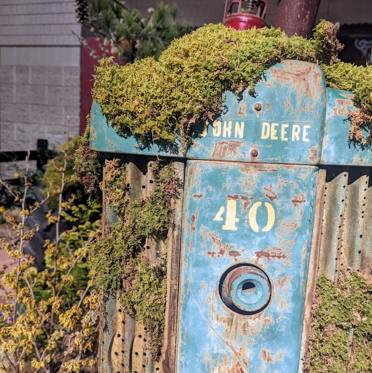 A light teal blue tractor with the words John Deere and the number 40 on them in white. It is nearly covered in moss.