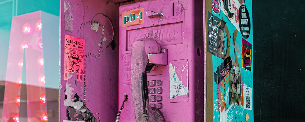 An old payphone that is spray-painted pink with grafitti and stickers all over it.