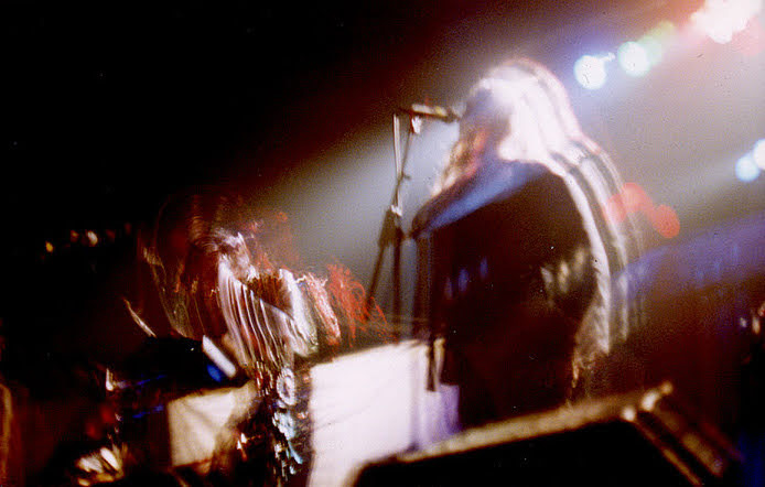 A couple people on stage during a concert. The exposure is a bit long leading to multiple ghost outlines of each person.