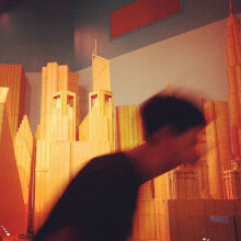 a blurry man walking in from of miniture cardboard buildings
