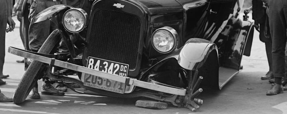 A very old car with a broken wheel, in black and white.