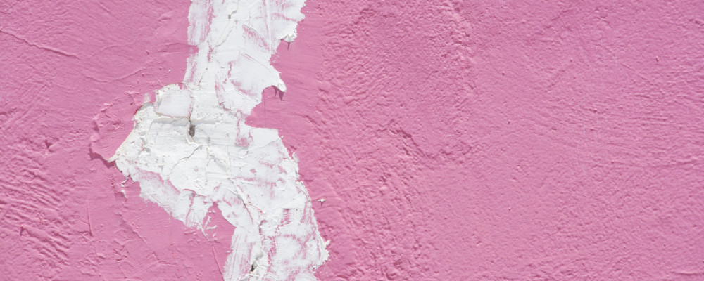 A close up of a wall panted pink with spackle filling in a large crack.